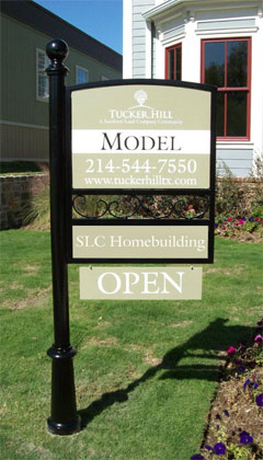 A green sign attached to a single black post identifying a model home at the Tucker Hill development
