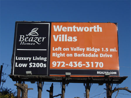 A red and black Beazer Homes billboard mounted on telephone posts