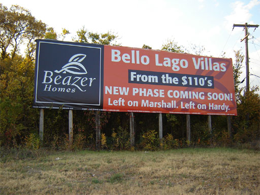 A long and narrow red and black billboard for Beazer Homes mounted on telephone posts