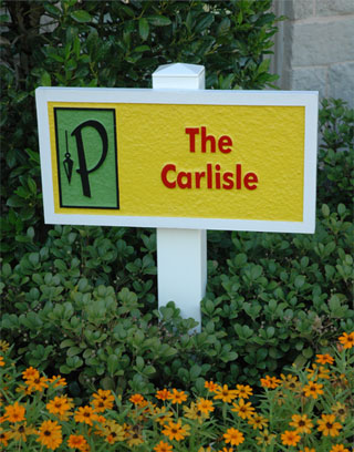 A small sandblasted and painted sign placedin a flower bed