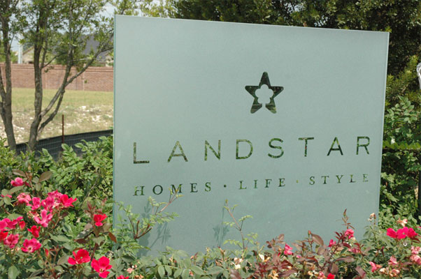 A large piece of frosted glass with an etched logo mounted in a flower bed