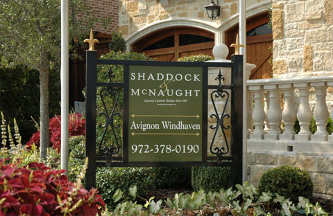 A green sign mounted in a black iron frame with decorative scrolls and pointed finials