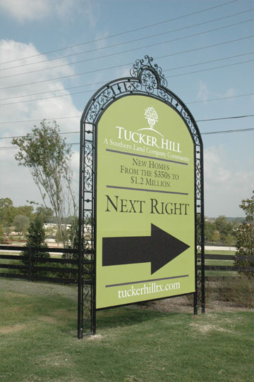 A large black and green directional sign with a large arrow pointing to the right in an elegant frame with scrollwork